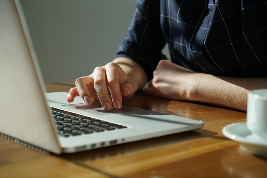 Person at desk using laptop, with drink mug nearby