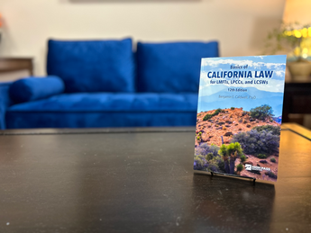 The book Basics of California Law for LMFTs, LPCCs, and LCSWs, 12th edition, on a book stand on a coffee table with a couch and lamp in the background.