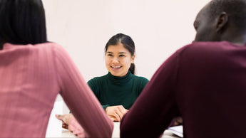 Woman smiling at a table with two people, one on each side, against a plain background