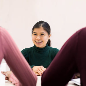 Woman smiling at a table with two people, one on each side, against a plain background